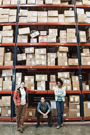 simsearch:6118-09174228,k - Team portrait of multi-ethnic female warehouse workers in a large distribution warehouse full of products stored on pallets in cardboard boxes on large racks. Fotografie stock - Premium Royalty-Free, Codice: 6118-09147891