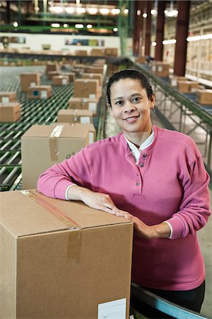 Portrait of an African American female warehouse worker in a large distribution warehouse with products stored in cardboard boxes. Stock Photo - Premium Royalty-Free, Code: 6118-09147894