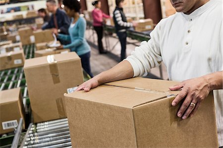 Team of multi-ethnic warehouse workers working on a motorized feed conveyor in a large distribution warehouse of products stored in  carboard boxes. Stock Photo - Premium Royalty-Free, Code: 6118-09147895