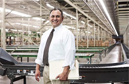 Portrait of a male Hispanic American executive in a shirt and tie surrounded by products stored in cardboard boxes  in a large distribution warehouse. Stock Photo - Premium Royalty-Free, Code: 6118-09147822