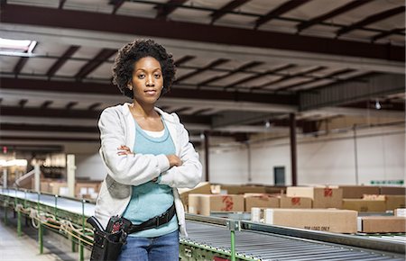 Portrait of an African American female warehouse worker in a large distribution warehouse with products stored in cardboard boxes. Stock Photo - Premium Royalty-Free, Code: 6118-09147835