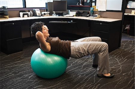 Caucasian woman working out on a Bosu Ball in her office cubicle. Stock Photo - Premium Royalty-Free, Code: 6118-09148099