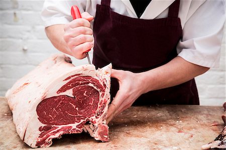simsearch:6118-08660016,k - Close up of butcher wearing apron standing at a wooden butcher's block, butchering beef forerib. Stock Photo - Premium Royalty-Free, Code: 6118-09148182