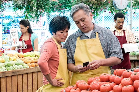 man and woman wearing aprons standing at stall with fresh tomatoes at a fruit and vegetable market. Stock Photo - Premium Royalty-Free, Code: 6118-09148131