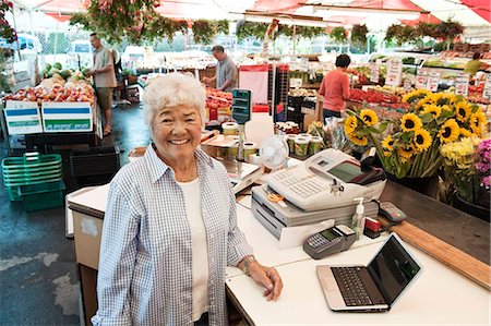 simsearch:6118-08762175,k - Senior woman standing at the checkout of a food and vegetable market, smiling at camera. Stock Photo - Premium Royalty-Free, Code: 6118-09148135