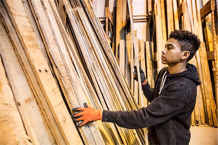 simsearch:6118-07121810,k - Young man wearing work gloves standing next to a stack of wooden planks in a warehouse. Foto de stock - Sin royalties Premium, Código: 6118-09148253