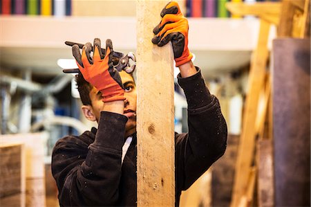 simsearch:6118-08947801,k - Young man wearing work gloves standing in warehouse, removing rusty nails from recycled wooden planks using pliers. Stock Photo - Premium Royalty-Free, Code: 6118-09148267