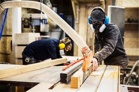 simsearch:6118-07121806,k - Man wearing ear protectors, protective goggles and dust mask standing in a warehouse, cutting piece of wood with circular saw. Stockbilder - Premium RF Lizenzfrei, Bildnummer: 6118-09148268