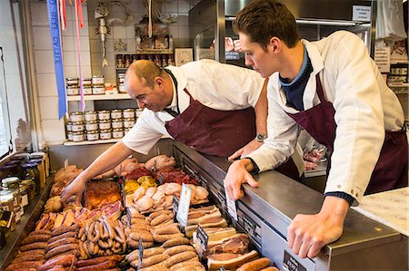 Two men wearing aprons standing at the counter of a butcher shop. Stock Photo - Premium Royalty-Free, Code: 6118-09148205