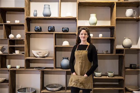 Woman with curly brown hair wearing apron standing in her pottery shop, smiling at camera. Foto de stock - Sin royalties Premium, Código: 6118-09148211