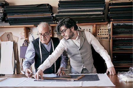 A tailor and a younger man, an assistant or apprentice working together, measuring cloth and cutting patterns. Stock Photo - Premium Royalty-Free, Code: 6118-09148341