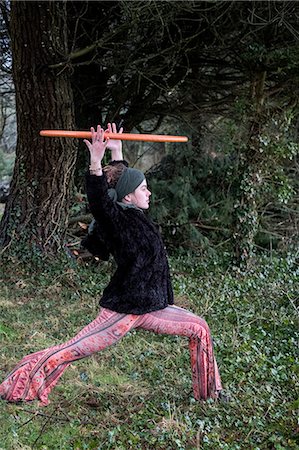 simsearch:6118-07731916,k - Young woman wearing floral trousers, black jacket and headscarf standing in forest, holding aloft hula hoop. Stockbilder - Premium RF Lizenzfrei, Bildnummer: 6118-09165846