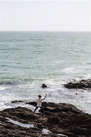 simsearch:6118-07731916,k - Young woman with brown hair and dreadlocks wearing white blouse standing on rocky shore by ocean, doing Tai Chi. Stockbilder - Premium RF Lizenzfrei, Bildnummer: 6118-09165825