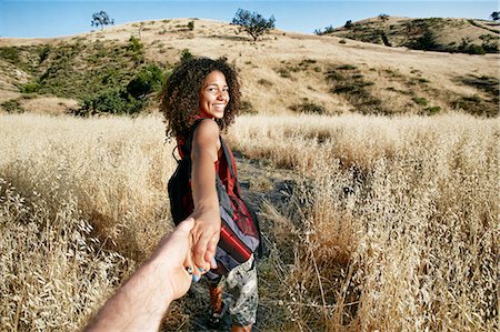 simsearch:6118-09165914,k - Young woman with curly brown hair hiking in urban park, holding man's hand. Foto de stock - Royalty Free Premium, Número: 6118-09165947