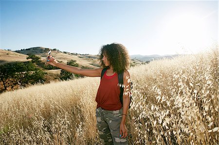 simsearch:6118-09165914,k - Young woman with curly brown hair hiking in urban park, taking picture with mobile phone. Foto de stock - Royalty Free Premium, Número: 6118-09165954