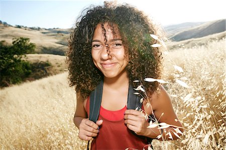 simsearch:6118-09165967,k - Young woman with curly brown hair hiking in urban park, smiling at camera. Foto de stock - Sin royalties Premium, Código: 6118-09165959