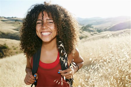 simsearch:6118-09165967,k - Young woman with curly brown hair hiking in urban park, smiling at camera. Foto de stock - Sin royalties Premium, Código: 6118-09165960