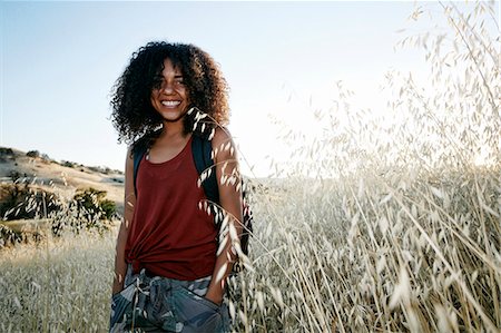 simsearch:6118-09165914,k - Young woman with curly brown hair hiking in urban park, smiling at camera. Foto de stock - Royalty Free Premium, Número: 6118-09165974