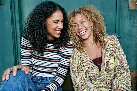 Portrait of two young smiling women with long curly black and blond hair, smiling and laughing. Stock Photo - Premium Royalty-Free, Code: 6118-09165925