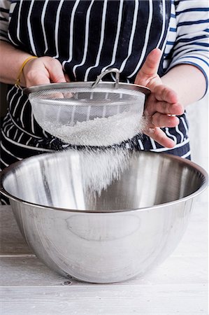 simsearch:6118-08971487,k - A cook sieving ingredients through a sieve, flour into a metal bowl. Stockbilder - Premium RF Lizenzfrei, Bildnummer: 6118-09166079