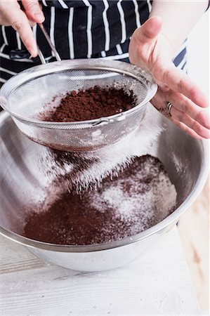 simsearch:6118-08971487,k - A cook sieving cocoa powder into a metal bowl of flour and cake ingredients. Stockbilder - Premium RF Lizenzfrei, Bildnummer: 6118-09166082