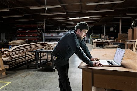 simsearch:6118-08088592,k - A Caucasian carpenter working on his lap top after hours in a large woodworking factory. Fotografie stock - Premium Royalty-Free, Codice: 6118-09166022