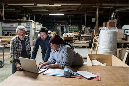 simsearch:6118-08088592,k - Three mixed race carpenters working on a laptop computer after work hours in a large woodworking factory. Fotografie stock - Premium Royalty-Free, Codice: 6118-09166026