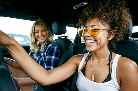 Portrait of two women with long blond and brown curly hair sitting in car, wearing sunglasses, smiling. Stock Photo - Premium Royalty-Free, Code: 6118-09166292