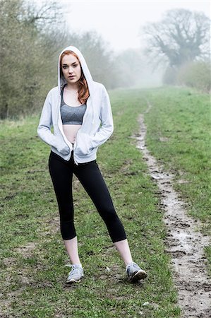 simsearch:6118-09165967,k - Young woman with long red hair wearing sports kit, exercising outdoors, looking at camera. Foto de stock - Sin royalties Premium, Código: 6118-09173444