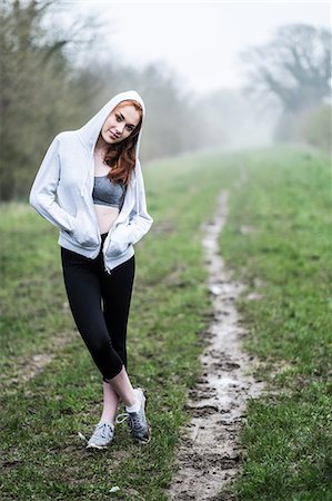 simsearch:6118-09165967,k - Smiling young woman with long red hair wearing sports kit, exercising outdoors, looking at camera. Foto de stock - Sin royalties Premium, Código: 6118-09173446