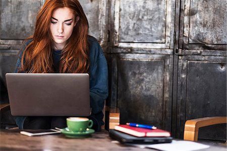 simsearch:649-08924663,k - Young woman with long red hair sitting at table, working on laptop computer. Foto de stock - Royalty Free Premium, Número: 6118-09173410