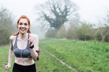simsearch:6118-09165967,k - Smiling young woman with long red hair wearing sports kit, exercising outdoors, looking at camera. Foto de stock - Sin royalties Premium, Código: 6118-09173433