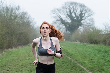 simsearch:6118-09165967,k - Young woman with long red hair wearing sports kit, exercising outdoors, looking at camera. Foto de stock - Sin royalties Premium, Código: 6118-09173434