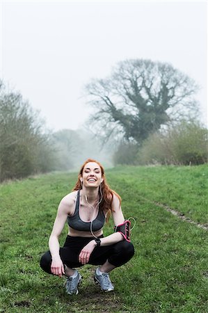 simsearch:6118-09165967,k - Young woman with long red hair wearing sports kit, exercising outdoors, looking at camera. Foto de stock - Sin royalties Premium, Código: 6118-09173435