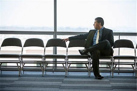 simsearch:6118-09173926,k - Hispanic businessman sitting in a row of chairs against a window in a conference centre lobby. Stock Photo - Premium Royalty-Free, Code: 6118-09173547