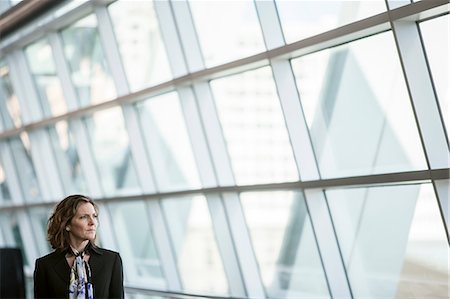 simsearch:6118-09173926,k - Caucasian businesswoman pausing for a moment near a large window in a conference centre lobby. Stock Photo - Premium Royalty-Free, Code: 6118-09173549