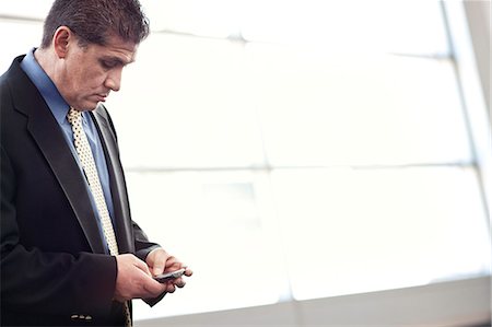 simsearch:6118-09173536,k - Hispanic businessman checking his cell phone in a conference centre lobby. Stockbilder - Premium RF Lizenzfrei, Bildnummer: 6118-09173533