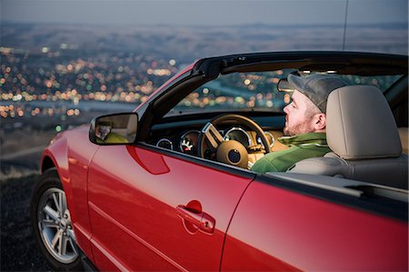 A Caucasian male parked in his convertible sports car watching the sunset over the Clearwater River and the city of Lewiston Idaho. Stock Photo - Premium Royalty-Free, Code: 6118-09173651