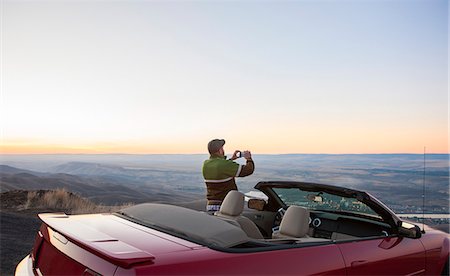 A driver stops to take a photograph at sunset near Lewiston, Idaho, USA on a road trip with his convertible sports car. Stock Photo - Premium Royalty-Free, Code: 6118-09173613