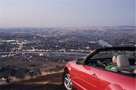 A Caucasian male parked in his convertible sports car watching the sunset over the Clearwater River and the city of Lewiston, Idaho, USA. Stock Photo - Premium Royalty-Free, Code: 6118-09173612