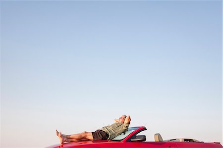 Caucasian male relaxing on the hood of his convertible sports car. Stock Photo - Premium Royalty-Free, Code: 6118-09173639