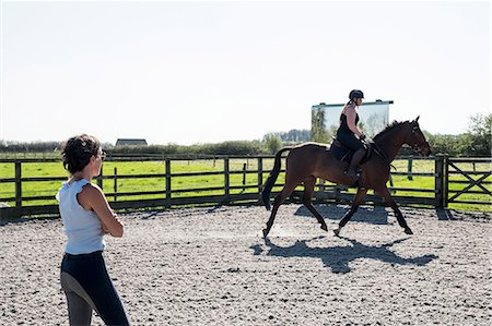 simsearch:6118-09173724,k - Woman, a horse trainer watching a young woman riding on a brown bay horse in a schooling ring. Stock Photo - Premium Royalty-Free, Code: 6118-09173726