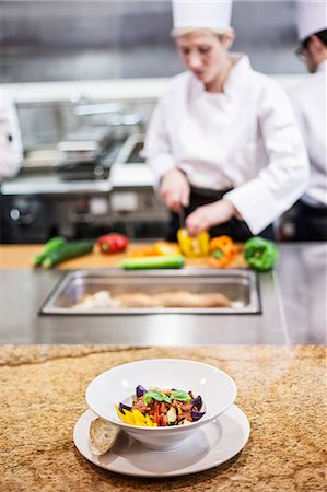 simsearch:6118-07808970,k - A closeup of a finished plate of food with chefs working in the background in a commercial kitchen, Stock Photo - Premium Royalty-Free, Code: 6118-09173943