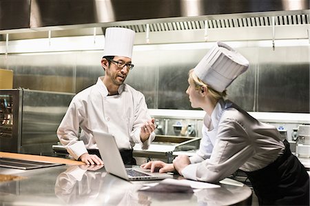 simsearch:614-08873482,k - A mixed race pair of chefs working with a laptop computer in a commercial kitchen. Fotografie stock - Premium Royalty-Free, Codice: 6118-09173952