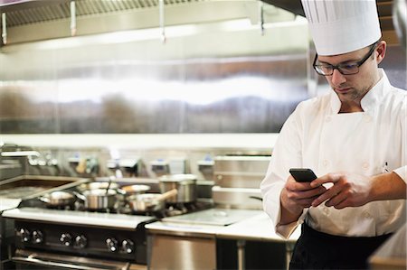 A Caucasian male chef checking his cell phone in a commercial kitchen, Photographie de stock - Premium Libres de Droits, Code: 6118-09173962