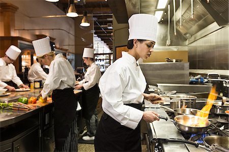simsearch:630-06723927,k - A crew of chef's working in a commercial kitchen, with a black chef in the foreground sauteing vegetables. Foto de stock - Sin royalties Premium, Código: 6118-09173967