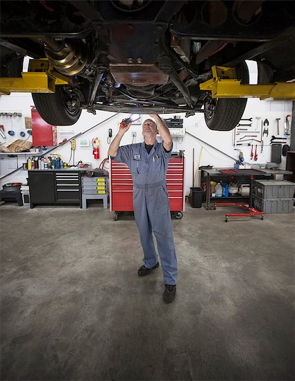 A Caucasian male mechanic working on the underside of a car in the shop. Foto de stock - Sin royalties Premium, Código de la imagen: 6118-09173987