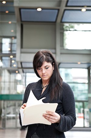 simsearch:6118-09173926,k - A young Caucasian businesswoman going through paperwork in a convention centre lobby area. Stock Photo - Premium Royalty-Free, Code: 6118-09173915