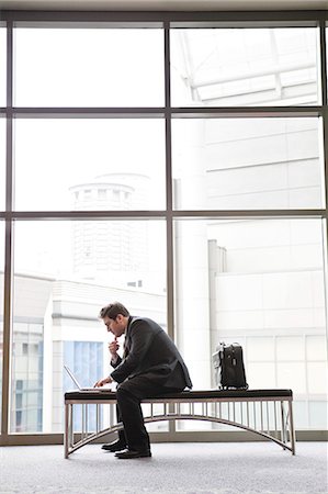 simsearch:6118-09173926,k - A businessman working on a laptop computer on a bench in a convention centre lobby Stock Photo - Premium Royalty-Free, Code: 6118-09173923