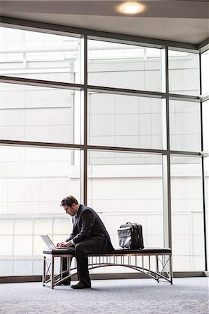 simsearch:6118-09173926,k - A businessman working on a laptop computer on a bench in a convention centre lobby Stock Photo - Premium Royalty-Free, Code: 6118-09173924